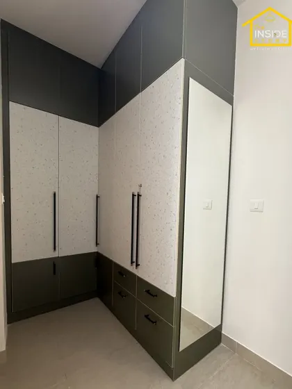 This corner wardrobe design makes the most of an L-shaped wall. The combination of dark green and a speckled white laminate, along with a full-length mirror, creates a stylish and highly functional storage solution.