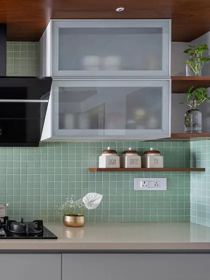 A close-up of the 'Gulmohar' kitchen palette, featuring mint green piccolo tiles, frosted glass cabinets, and open wooden shelves for a light and airy feel.