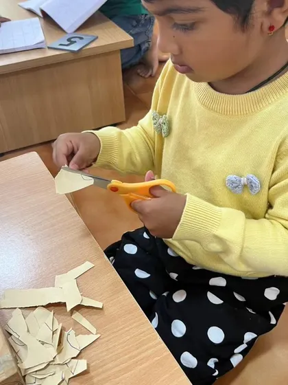 A child practices her cutting skills. This practical life activity requires immense concentration and develops the hand strength and coordination necessary for writing and other tasks.