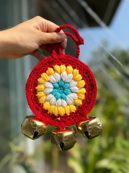 A red ghungroo hanging with a central floral motif in yellow, white, and blue. A very traditional and vibrant design.