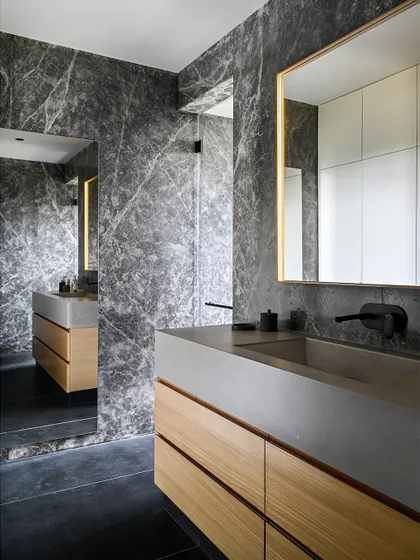 The dramatic grey marble wall cladding provides a stunning backdrop for the minimalist concrete sink and wooden drawers.