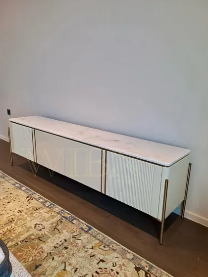 A custom TV console with a white marble top, fluted and smooth door panels, and delicate metal legs. This piece was delivered to a client's home, adding a touch of refined elegance to their bedroom.