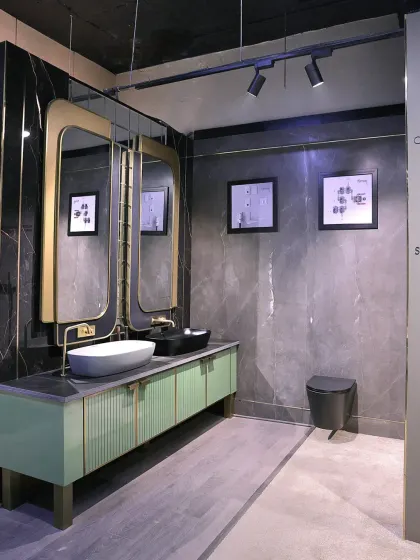 This display features a mint green vanity with ribbed detailing and unique gold-framed mirrors, set against a dark, moody tile.