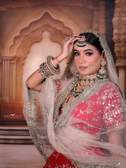 A classic bridal pose, with the bride adjusting her veil. The soft, sheer fabric of the dupatta creates a dreamy effect, framing her face beautifully.
