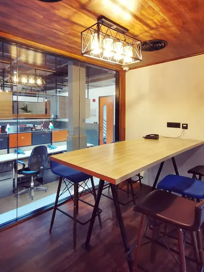 A small, high-table meeting area adjacent to the main workspace. These informal zones are crucial for quick discussions and collaborative work without needing to book a formal room.