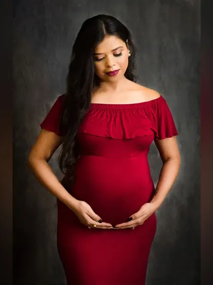 A classic standing pose that beautifully showcases the baby bump. The off-shoulder red gown and the simple, dark background create an elegant and timeless maternity photograph.