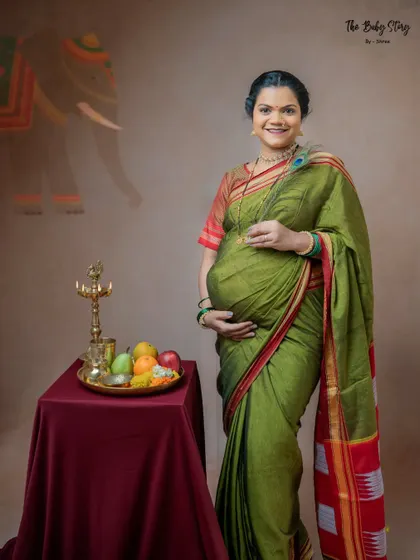 A standing portrait where the mom-to-be holds a peacock feather. The background subtly features an elephant motif, adding another layer of cultural symbolism to this traditional maternity photo.