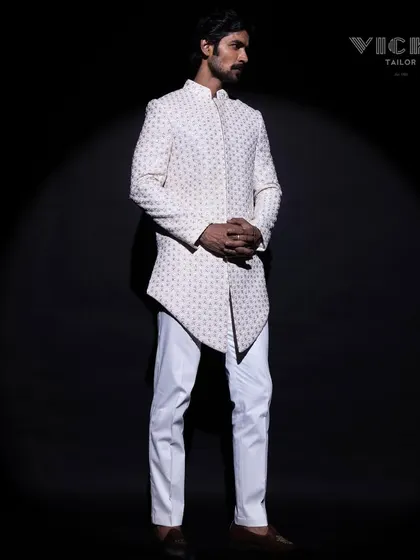 Modern architecture in tailoring. This white sherwani features a striking asymmetric hemline and all-over geometric embroidery, crafted for the groom who appreciates contemporary design.