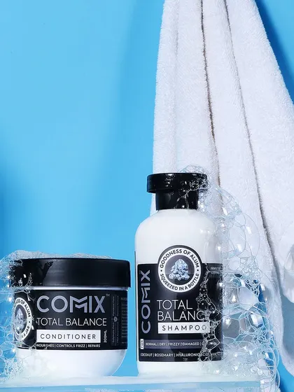 A bathroom shelf scene for a shampoo and conditioner set. The bubbles and hanging towel create an authentic, 'just used' feel, making the products seem effective and refreshing.