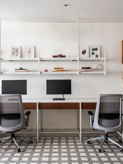 The main workstation area in the 'On The Grid' office is designed for efficiency and collaboration. We used white metal desks with marble tops and ceiling-suspended open shelves to maintain a clean, airy aesthetic, ensuring the 700 sq. ft. space feels uncluttered and productive.