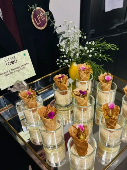 Edamame and Asparagus Cornetto with Crispy Leeks. This appetizer features a savory filling in a delicate cone, garnished with edible flowers, and is presented on a tray by our professional server for a touch of elegance.