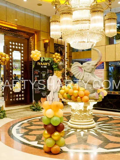 The lobby of a venue transformed into a jungle, with animal-themed balloon columns and a large elephant statue centerpiece.