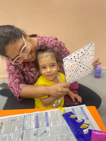 A mother and her smiling son hold up a kite they decorated, showing their pride in their joint creation.