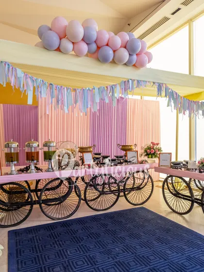 A charming food and drink station with vintage-style carts, pastel draping, and a soft balloon garland overhead.