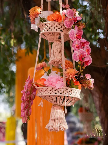A beautiful two-tiered macrame hanging planter filled with pink orchids and other colorful flowers.