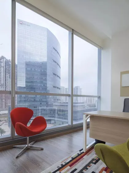 A private cabin in the CorporatEdge office with a stunning view of the Gurugram skyline. The minimalist design and statement red chair create a powerful yet uncluttered workspace for focused tasks.