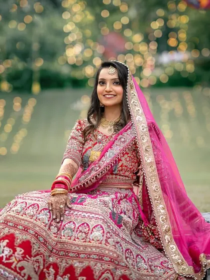 A stunning bridal portrait. The bride, in her vibrant pink lehenga, sits gracefully in a garden with a beautiful bokeh background.