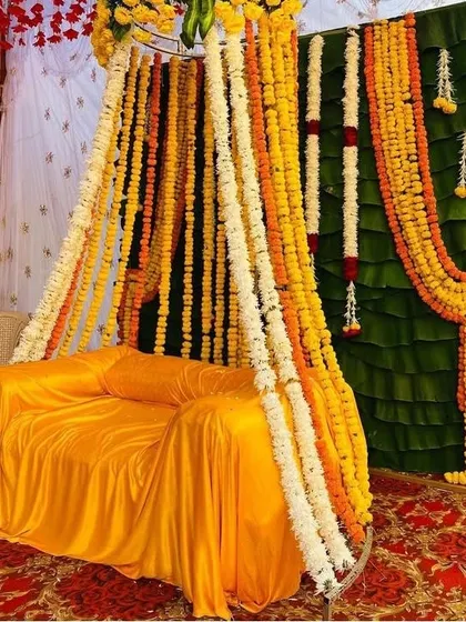 A traditional Haldi seating area with a sofa covered in yellow fabric, set against a backdrop of banana leaves and dense marigold garlands.