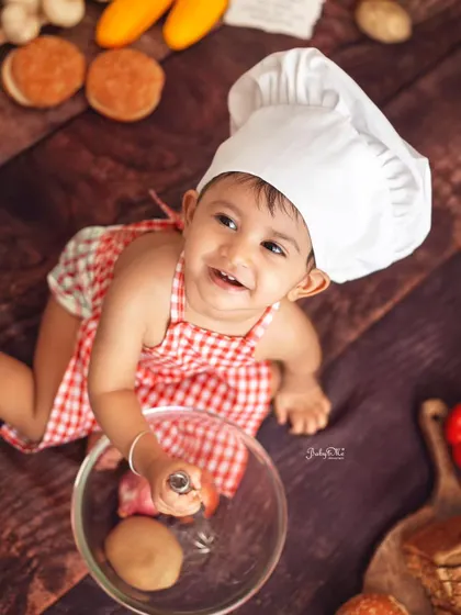 Looking up with the sweetest, most mischievous smile. The overhead angle captures the fun of playing with the mixing bowl and ingredients.