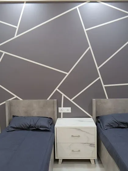 A shared bedroom designed with a modern geometric pattern on the wall. The twin beds and minimalist nightstand make it a stylish and functional space for siblings.