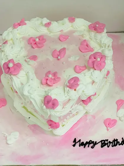A lovely heart-shaped cake with pink floral details, perfect for a birthday.