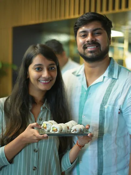 A couple proudly presents their finished plate of sushi rolls. Our workshops are a great activity for partners to learn and create something delicious together.