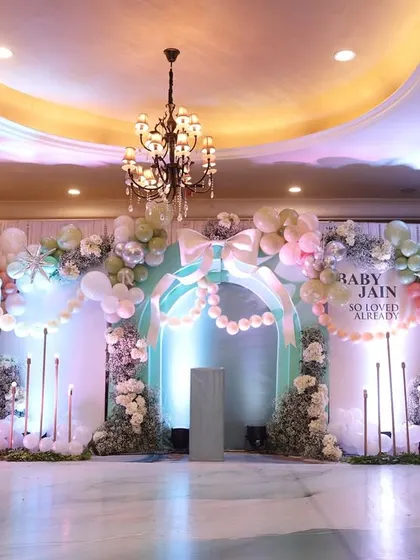 A grand and ethereal stage setup for Baby Jain's shower, with pastel balloon arches, white florals, and elegant lighting.