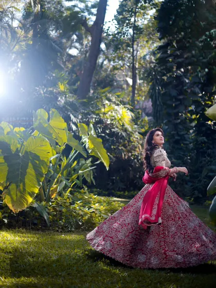 A wide shot of Mahima in a beautiful garden. Her makeup and outfit create a striking image against the lush greenery, showcasing a look that is both grand and connected to nature.