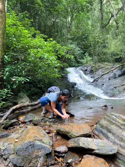 A trekker refreshes herself with cool, clear water from a mountain stream. I guide teams to these pristine spots for a pure nature experience.