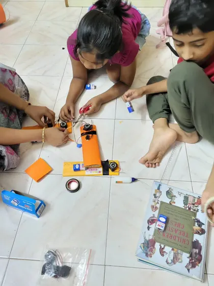 Students work together on the floor, focused on wiring their electronic models.