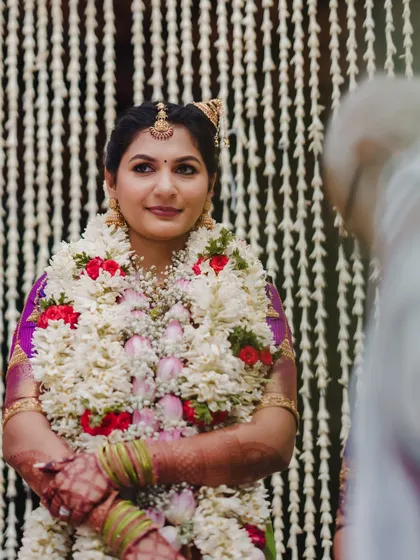 The bride, adorned with heavy floral garlands, listens intently during the wedding rituals. The decor is designed to frame her beautifully without overwhelming the moment.