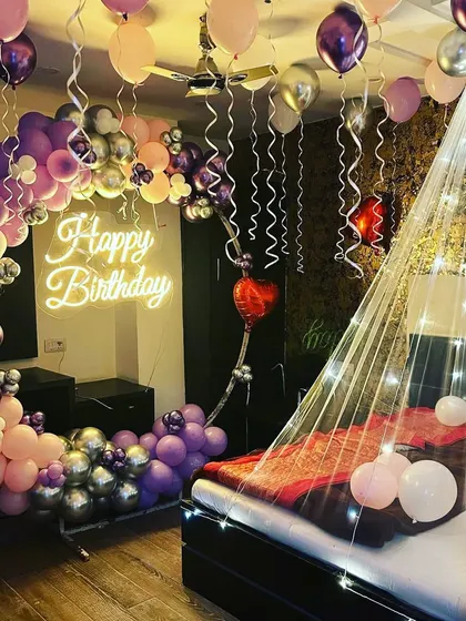 Another view of a romantic birthday room, showing the full effect of the crescent moon balloon arch, neon sign, and the bed canopy with fairy lights.