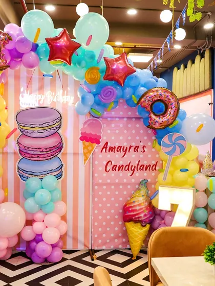 A full view of our "Candyland" themed decor for a 7th birthday. The setup includes a custom backdrop, a light-up number, and elaborate balloon sculptures of donuts, macarons, and ice cream.