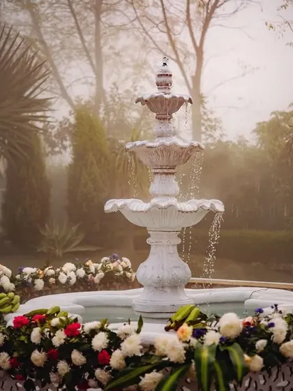 A serene white fountain surrounded by flowers, a beautiful and tranquil feature at the South Indian wedding venue.