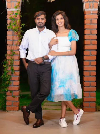 A stylish and modern pre-wedding photo of a couple posing between two brick pillars at night.