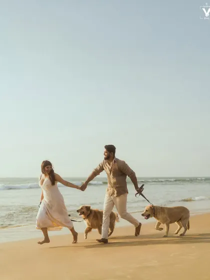 A dynamic shot of a couple running along the shoreline, holding hands while walking their two excited golden retrievers. This action shot captures the fun and energy of a beach pre-wedding session with pets.