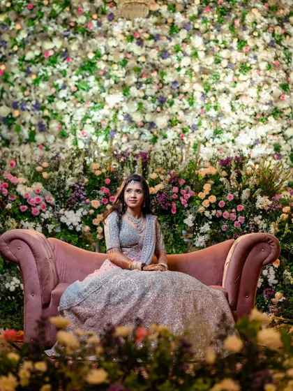 A beautiful portrait of the bride seated on a pink sofa against a wall of flowers at her reception.