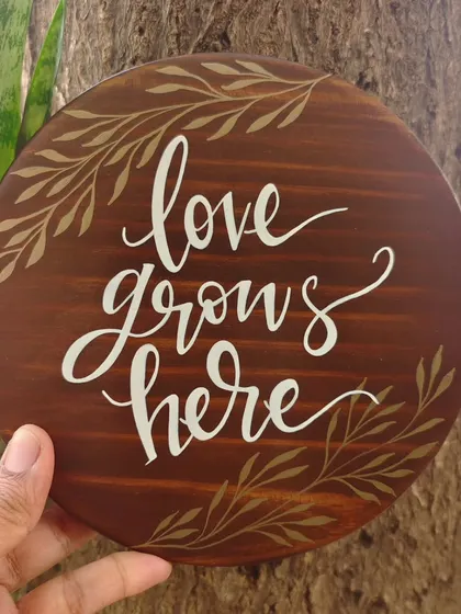 The "love grows here" plaque placed against a tree trunk, emphasizing the natural, earthy feel of our wooden decor.