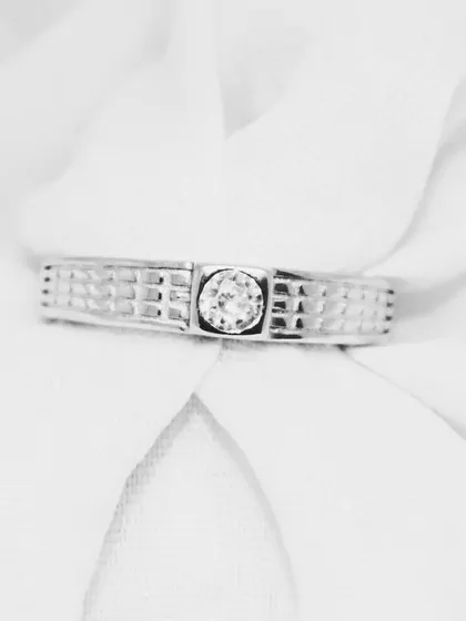This close-up on a soft background showcases the fine details of the band ring, from the grid-like texture to the secure setting of the solitaire.