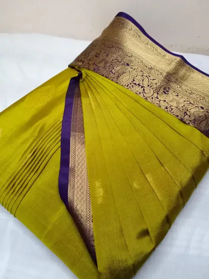 An olive green saree with a rich purple and gold border. It has been pleated and box folded, making it easy to store and travel with.