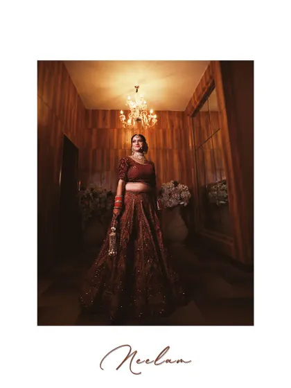 A full-length bridal portrait in a beautifully lit, wood-paneled room. The bride stands elegantly under a chandelier, creating a classic and sophisticated image.