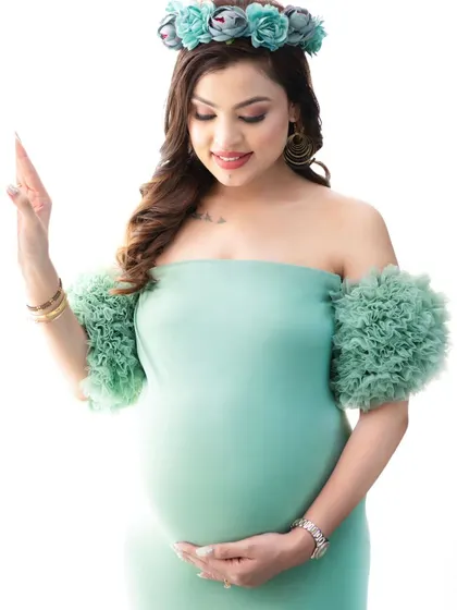 A simple, elegant portrait against a clean white background. The focus is entirely on the mother-to-be, her mint green gown, and the gentle way she cradles her baby bump.