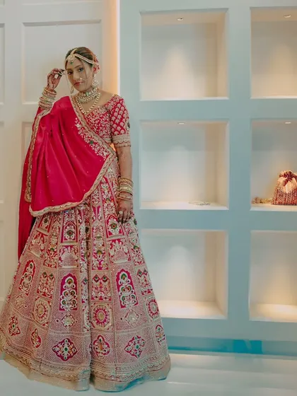 A stunning full-length portrait of the bride in her red lehenga, posing against a modern, minimalist background.