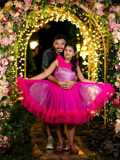 A happy couple posing under a floral arch. The bright lights and flowers create a wonderfully romantic setting for a pre-wedding night shoot.