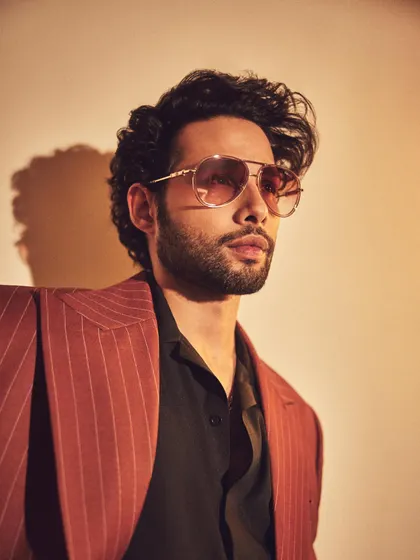 A close-up of Siddhant Chaturvedi in a custom pinstripe suit. The tinted aviator glasses add a cool, retro vibe to the sharp tailoring.
