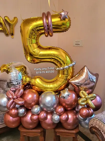 A 5th birthday setup featuring a large number '5' balloon bouquet and helium balloons floating on the ceiling.
