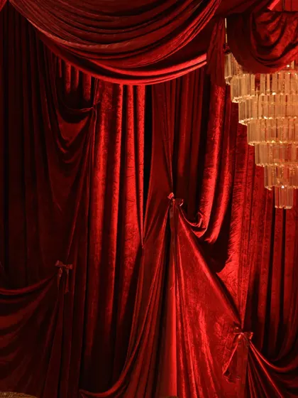 A detail shot of the luxurious red velvet drapes, tied back to reveal the layers of fabric. The quality of the material and the way it hangs is central to creating this opulent look.