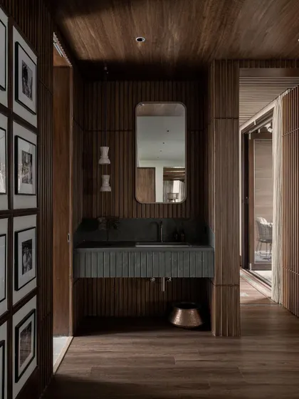The beautiful wood-clad powder room at Pràna, where every detail is considered. The fluted vanity and gallery wall create a space that is rich in texture and personality.