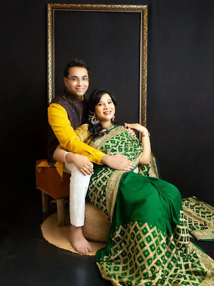 A power couple portrait in traditional green and yellow attire. The pose is confident and elegant, set against a classic framed backdrop.