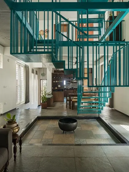 A staircase should be more than just a utility; it can be the heart of a home. This suspended metallic staircase in 'Jodi Mane' is a functional sculpture, adding a bold splash of color and creating dynamic shadow play from the ample daylight.